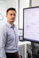 Trainer in einem hellen Entwicklerbüro neben einem Bildschirm mit Git- und Cloud-Arbeitsabläufen
